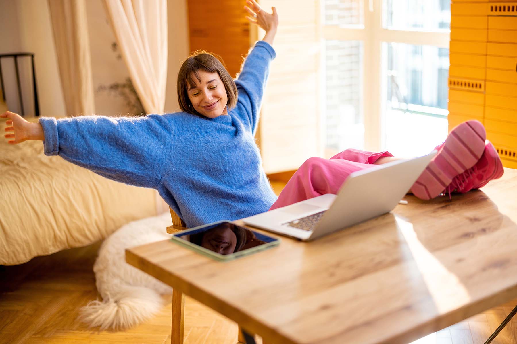 A woman stretching with joy at a table with a laptop.