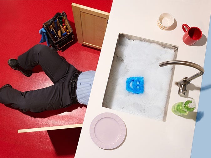 Overhead view of a plumber lying beside a tool bag and a sink filled with soapy water