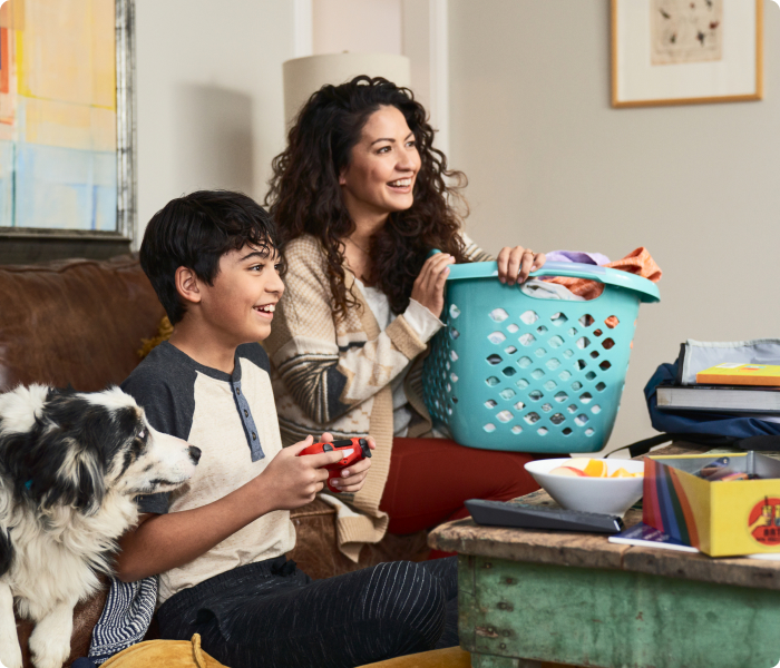 Woman holding laundry basket while son plays video game