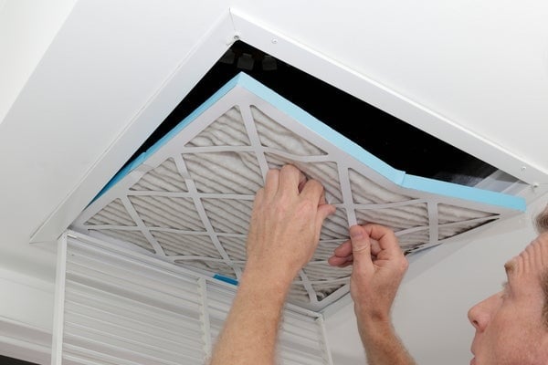 Person removing an old dirty air filter from a ceiling intake vent of a home HVAC system.