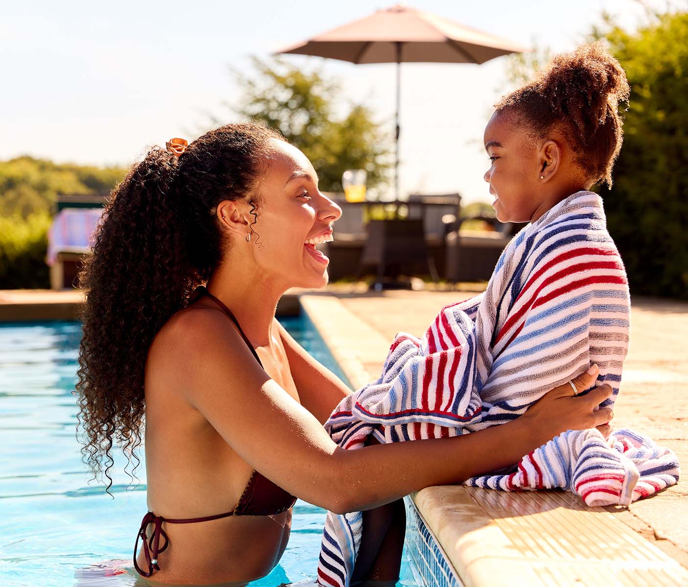 A laughing woman wraps a child in a towel poolside