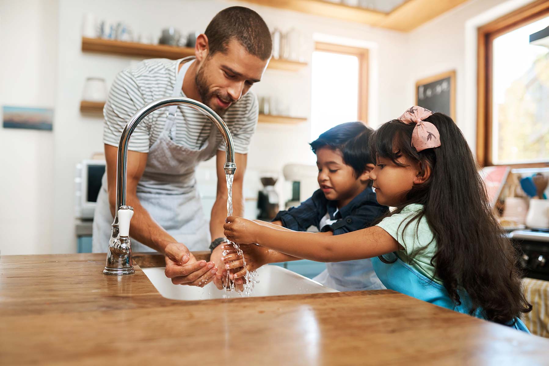 A man and two children wash hands at a kitchen sink