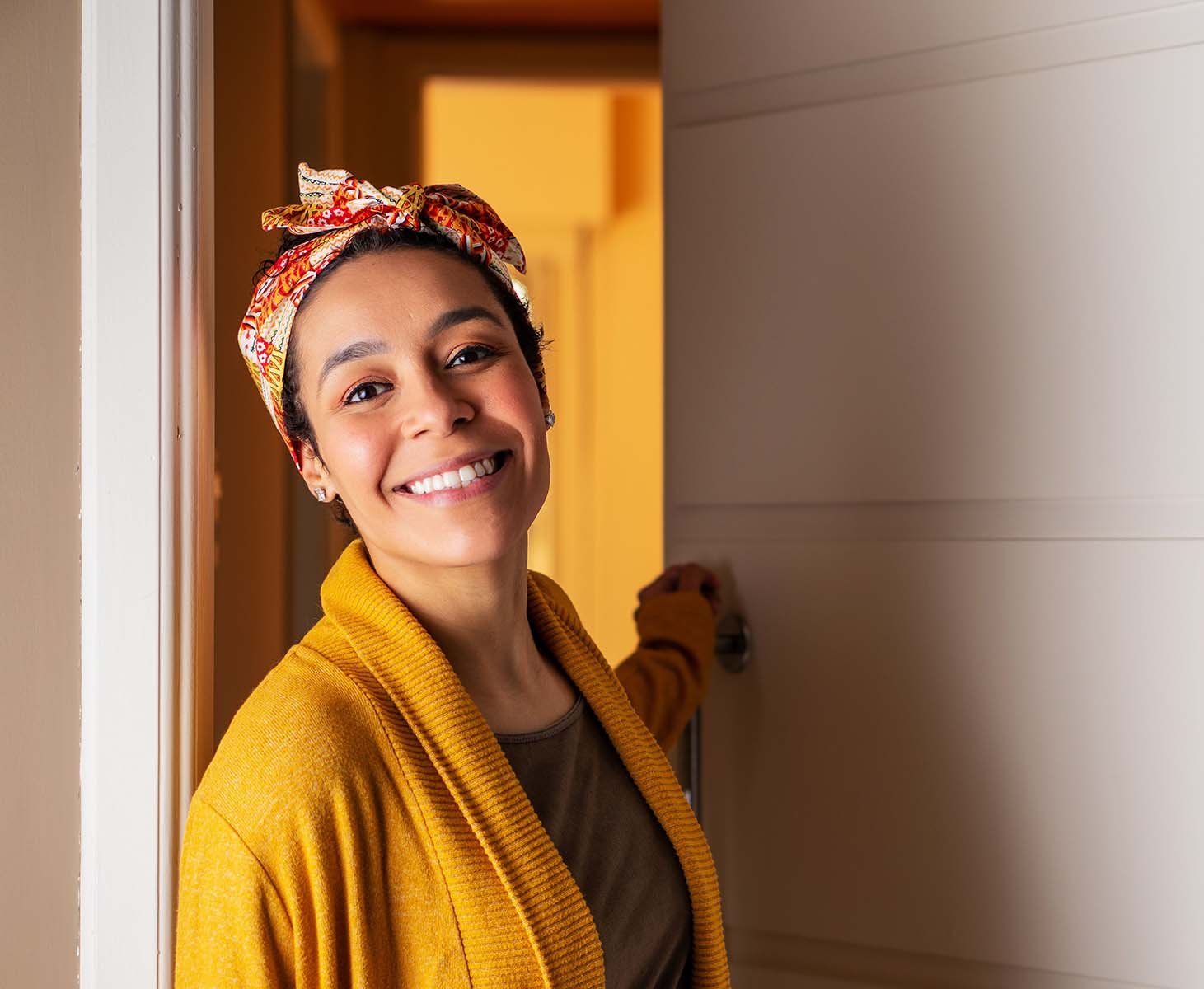 A smiling woman in a yellow headwrap and sweater.