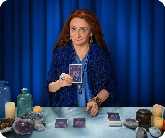 Tarot reader holding an AHS Tarot card in front of a blue curtain